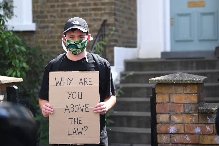 A protestor with a sign reading 'why are you above the law?'
