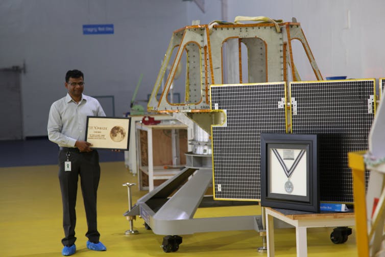 man holding plaque beside a model of a robotic spacecraft