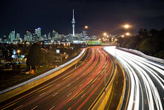Vehicle lights blur at night on a busy motorway into Auckland.