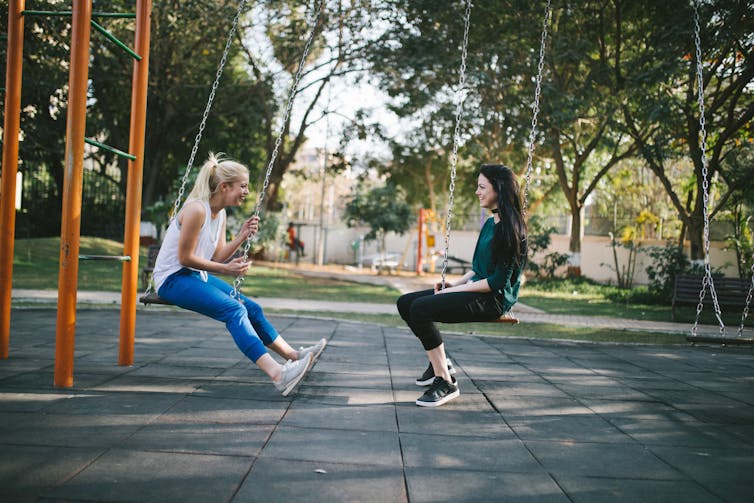 Two girls sitting on swings and chatting.