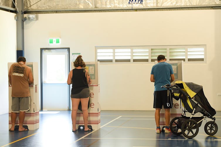 People voting at polling booths in school hall.