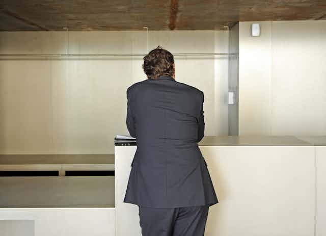 Un hombre de traje, de espaldas, apoyado en un mostrador vacío.