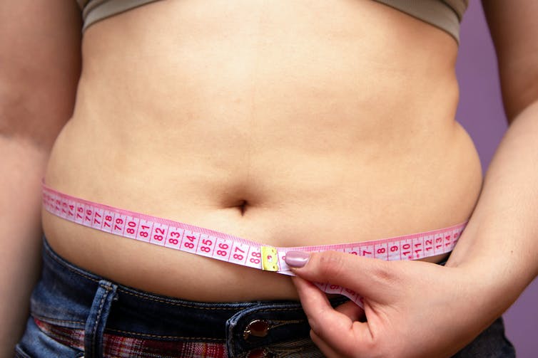 Overweight woman holds a tape measure around her waist.