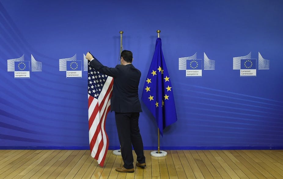 Un employé du Parlement européen accroche les drapeaux américain et européen