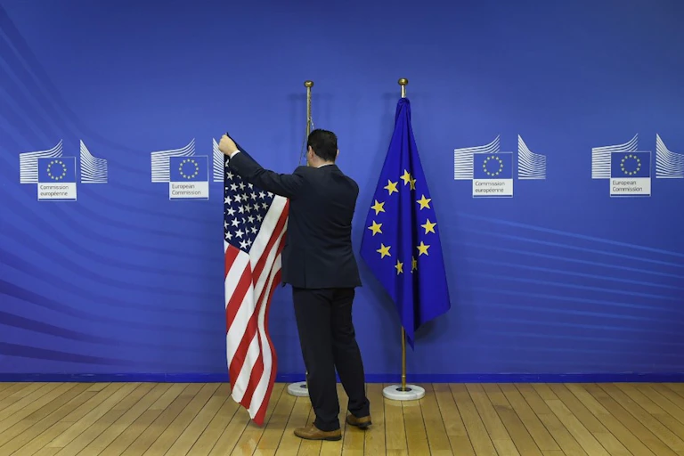 Un employé du Parlement européen accroche les drapeaux américain et européen