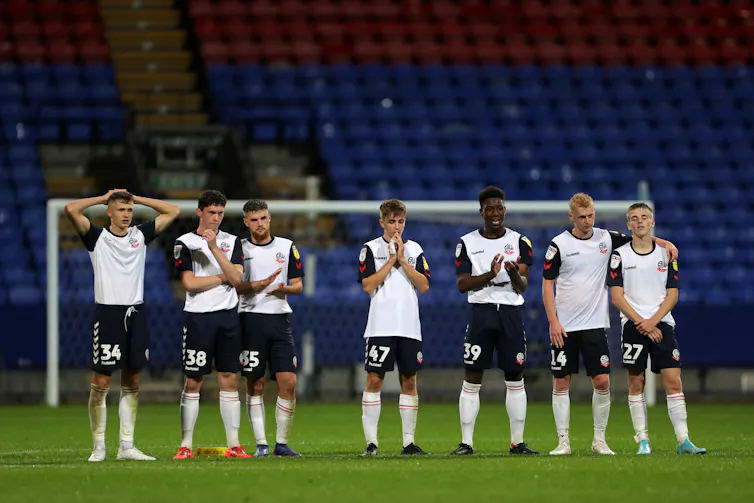 Seven Bolton Wanderers football players stand in line in front of empty stadium.