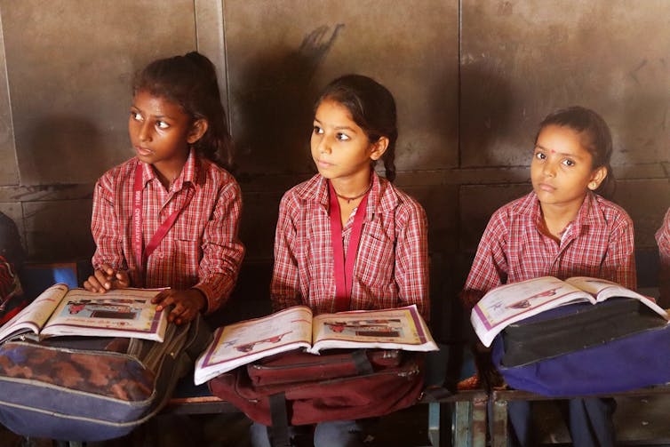 Three schoolgirls sitting at desks with textbooks open.