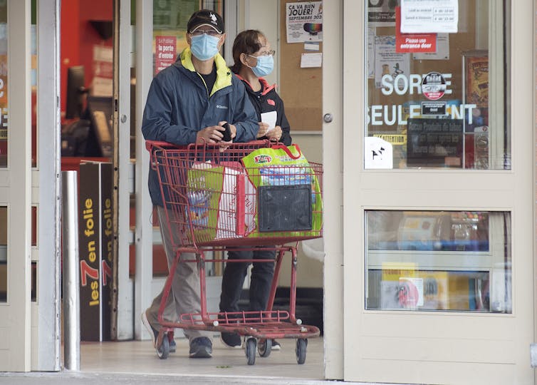 People wear face masks as they leave a grocery store pushing a cart.