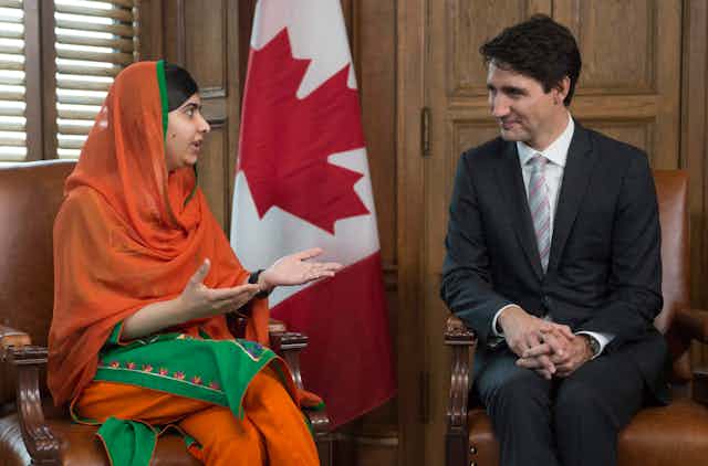 Malala Yousafzai gestures as she speaks to Justin Trudeau. A Canadian flag is behind them.