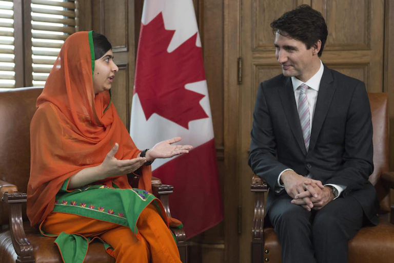 Malala Yousafzai gestures as she speaks to Justin Trudeau. A Canadian flag is behind them.