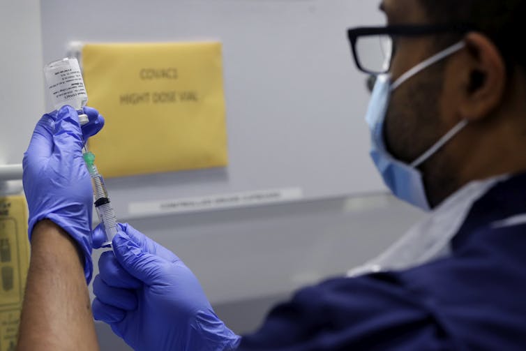 A man wearing a face mask and gloves preparing a syringe for injection.