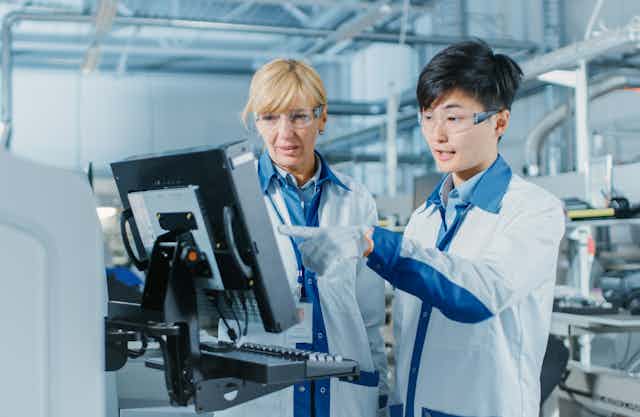 Young male engineer talks with female supervisor while looking at computer screen in high-tech factory