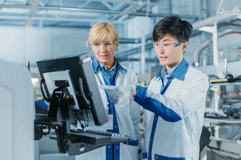 Young male engineer talks with female supervisor while looking at computer screen in high-tech factory