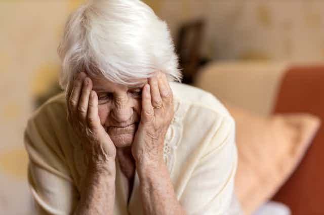 An old woman holds her head in her hands.