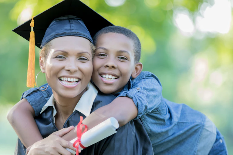 A woman wearing a graduation cap is being hugged by her young son.