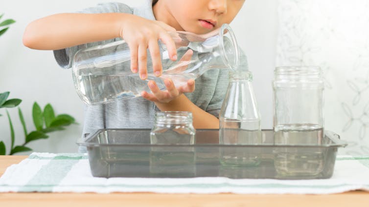 A boy pouring water from one glass bottle to another.