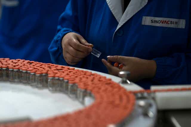 Orange-capped vials on a conveyor belt. A worker holds several vials in their hands. 