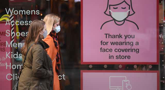 Shoppers wearing face masks pass a COVID-19 awareness sign on a high street in England