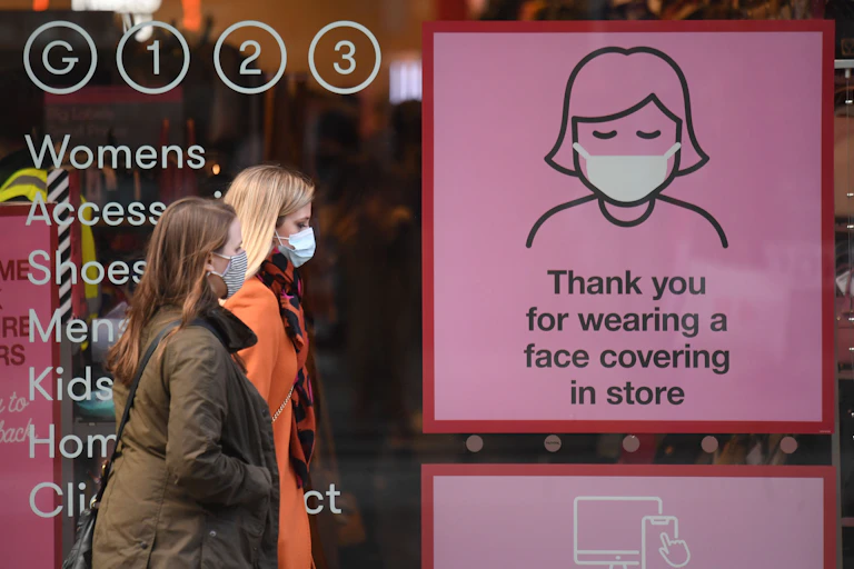 Shoppers wearing face masks pass a COVID-19 awareness sign on a high street in England