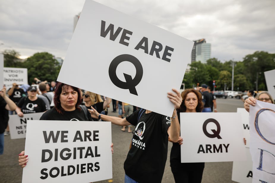 People display Qanon messages on cardboard signs at a political rally.