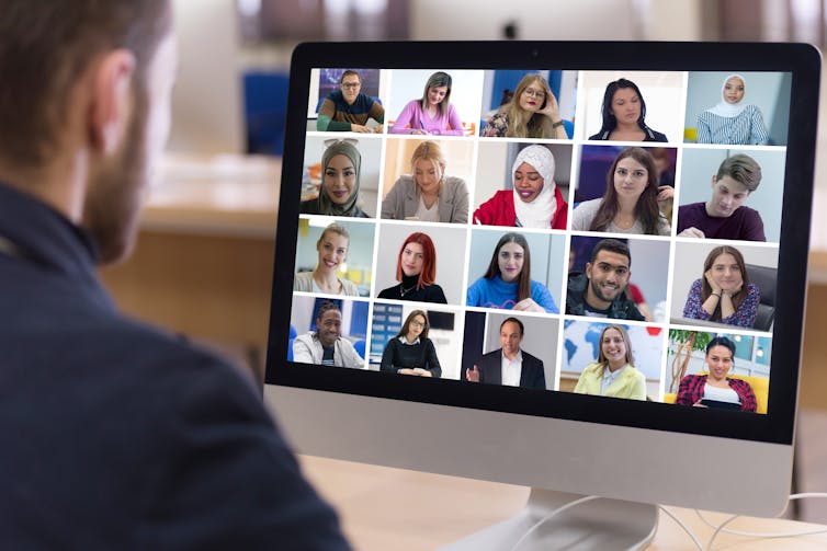 Man looking at screen of video call with numerous others on screen