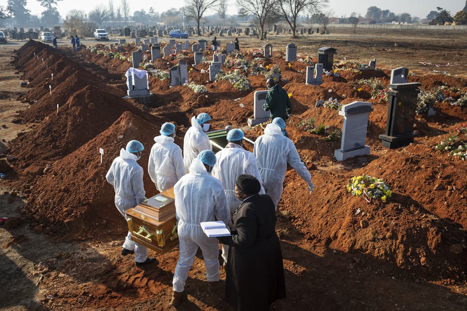 Six men wearing white protective gear carry the coffin of a COVId-19 victim at a cemetery in South Africa