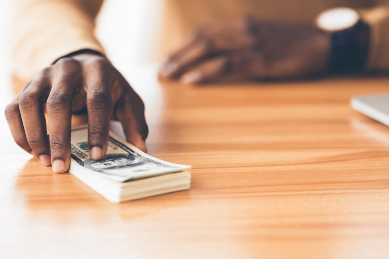 A hand placing a stack of paper money on a table