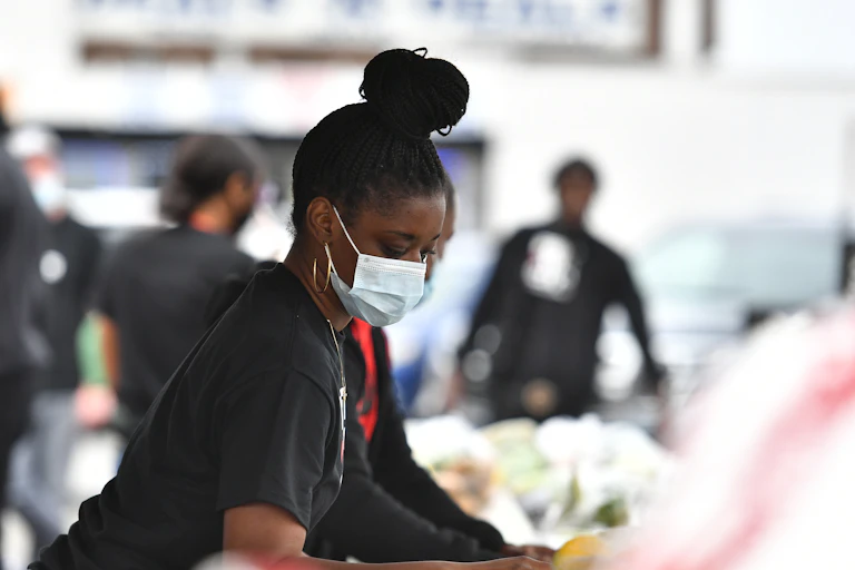 A woman in a mask leans over a pile of stuff.