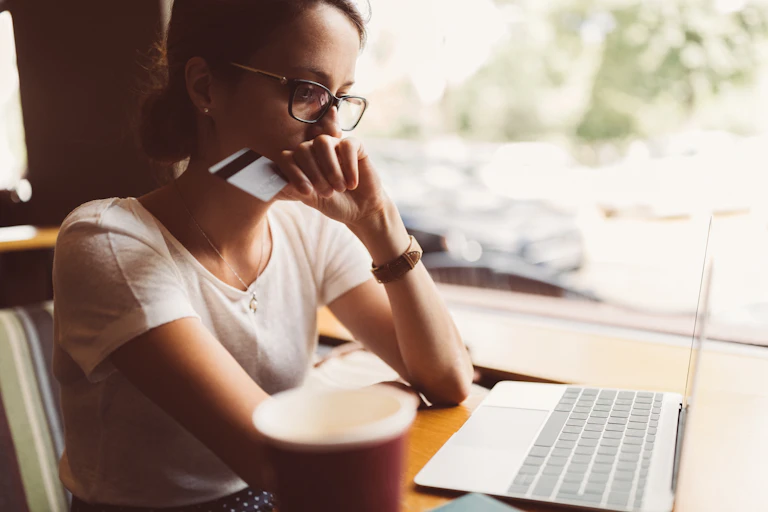A woman staring intently at a laptop screen while holding a credit card