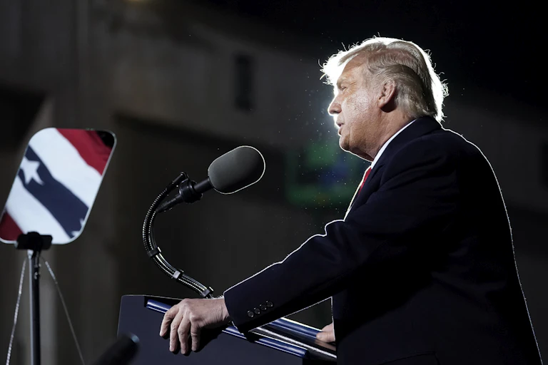 Trump stands in front of a podium, the American flag reflected in the teleprompter in front of him.