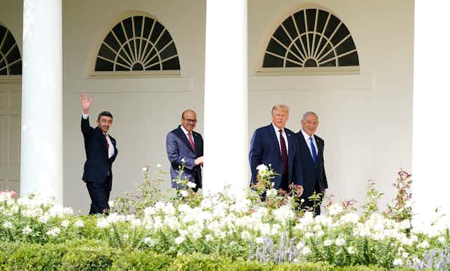 Donald Trump walks to the Abraham Accords signing ceremony at the White House with Israeli Prime Minister Benjamin Netanyahu, Bahrain Foreign Minister Khalid bin Ahmed Al Khalifa and United Arab Emirates Foreign Minister Abdullah bin Zayed al-Nahyan. Shrubs with white flowers are in the foreground.