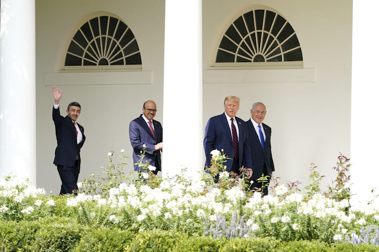 Donald Trump walks to the Abraham Accords signing ceremony at the White House with Israeli Prime Minister Benjamin Netanyahu, Bahrain Foreign Minister Khalid bin Ahmed Al Khalifa and United Arab Emirates Foreign Minister Abdullah bin Zayed al-Nahyan. Shrubs with white flowers are in the foreground.