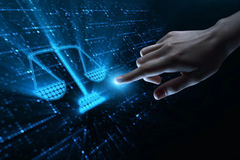 A finger points to a screen with a blue digital icon of the scales of justice on a dark background