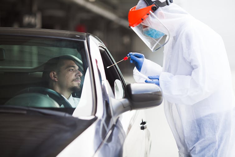 A health worker dressed in PPE prepares to take a swab from a man in his car.