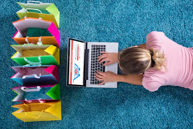 Una mujer tumbada ante un ordenador y varias bolas de compra de colores vivos.