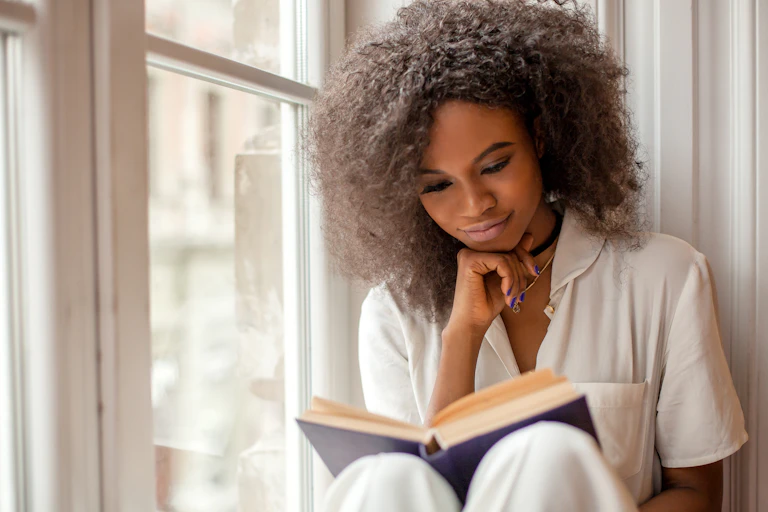 Girl reading a book in a window alcove.
