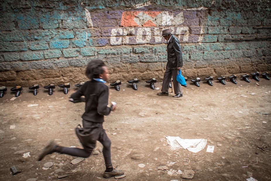 A school girl runs past an old man walking along a street with shoes for sale