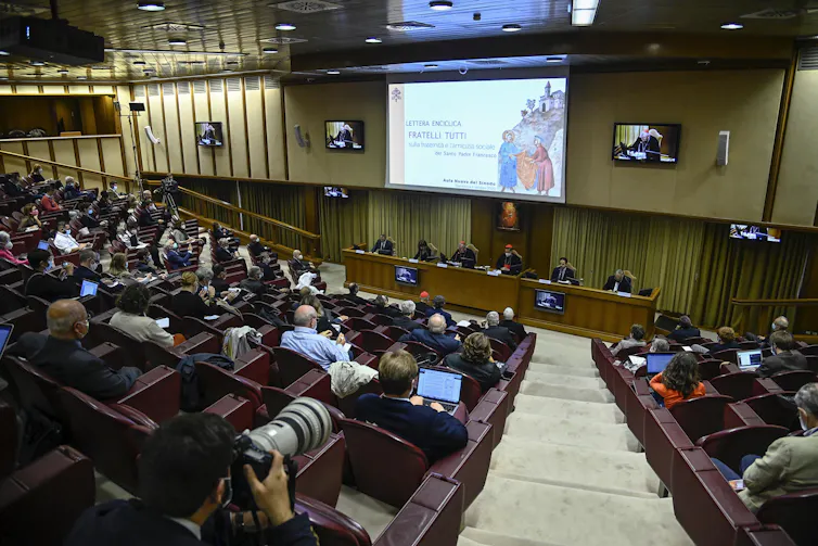 A penal of six people presenting the papal encyclical to a group of people in an auditorium in Rome.