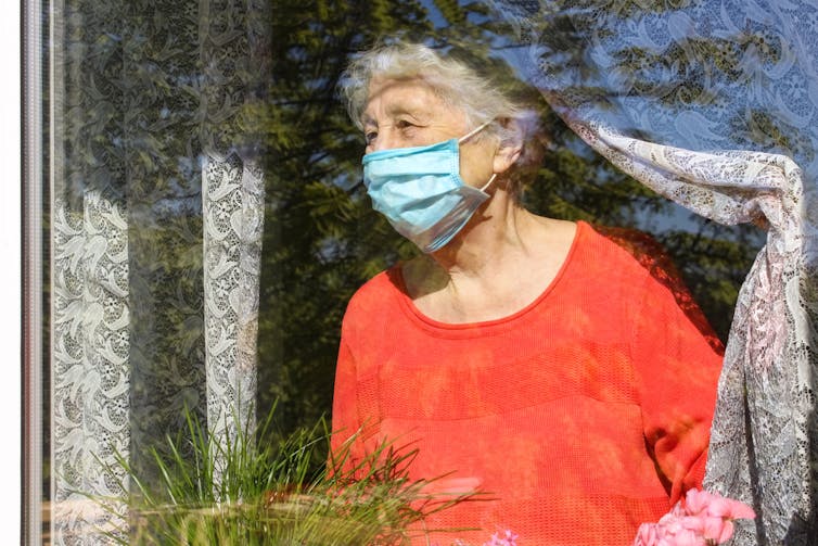 An elderly lady wearing a face mask stairs out of the window.