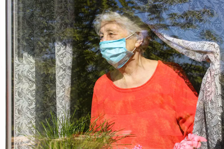 An elderly lady wearing a face mask stairs out of the window.