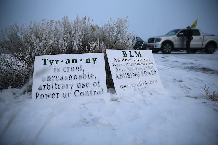 Protest signs in snow with protesters in background.