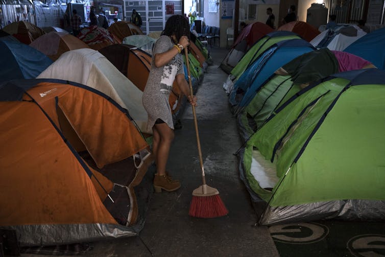 A woman sweeps the concrete floor amid rows of tents