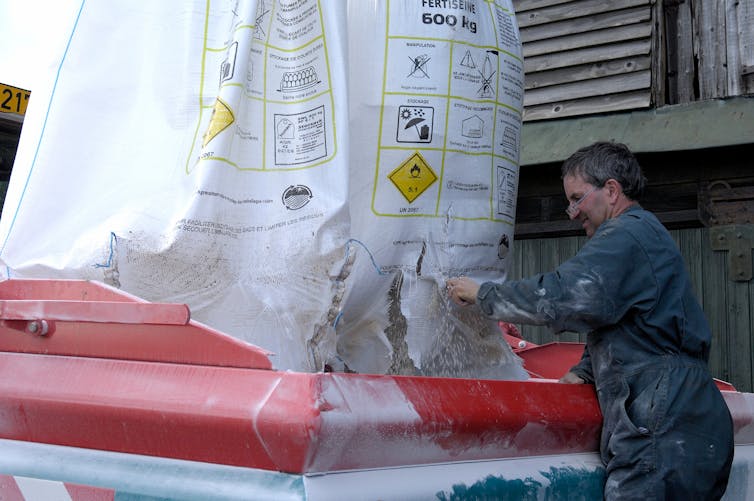 A farmer emptying fertiliser into machinery