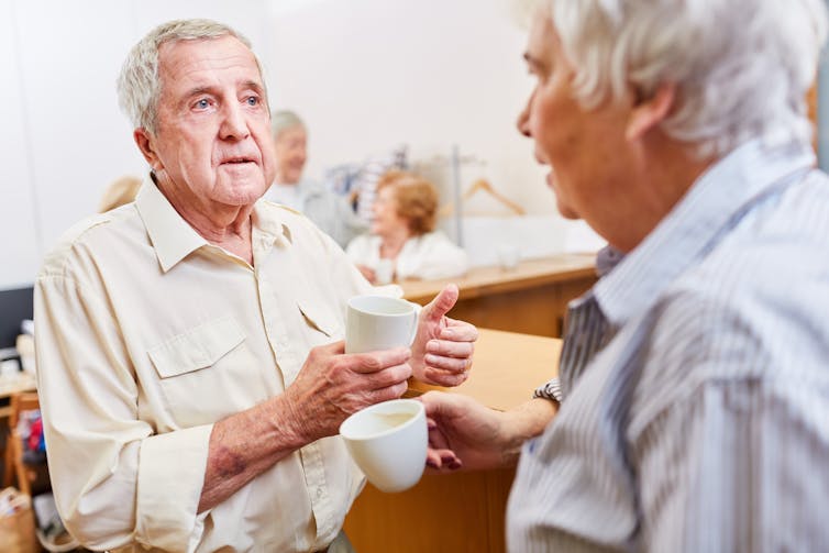 Two elderly men talking over a cup of coffee in an aged-care setting.