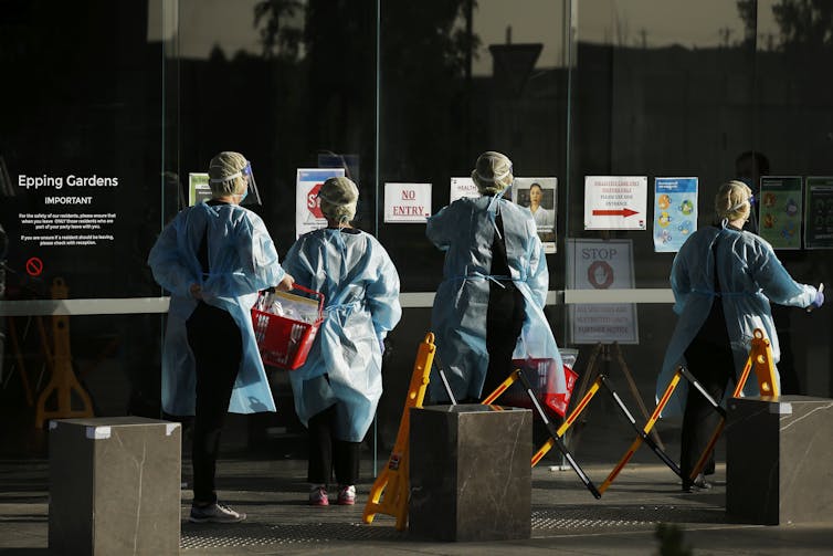Health-care workers wearing PPE outside an aged-care home.