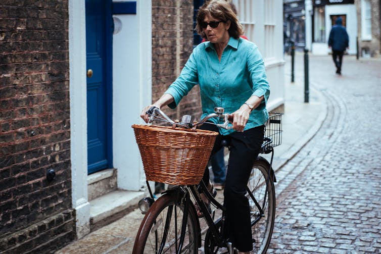 一位妇女骑着自行车经过一所房子，前面放着一个柳条篮子。