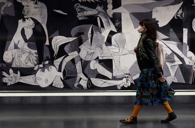 A woman wearing a mask walks past Picasso's painting Guernica