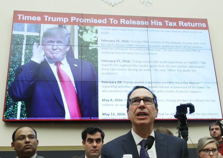 Treasury Secretary Steven Mnuchin testifies during a House Financial Services Committee on May 22, 2019. A screen behind him displays President Trump and a list of times he has promised to release his tax returns.