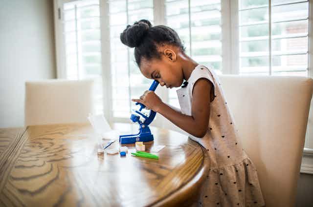 Young girl looks into blue microscope on table.