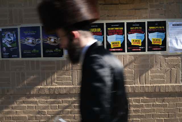 An ultra-Orthodox Jewish man walks past poasters calling on people to wear face masks.